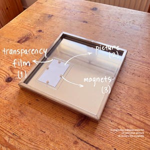Magnetic metal photo frame with a small vertical print on transparency film, held by four magnets.