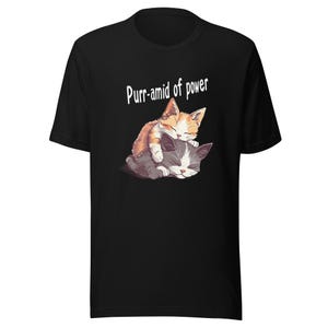 May include: Black t-shirt with a graphic of two sleeping cats, one ginger and white, the other grey and white. The text "Purr-amid of power" is printed above the cats in white.