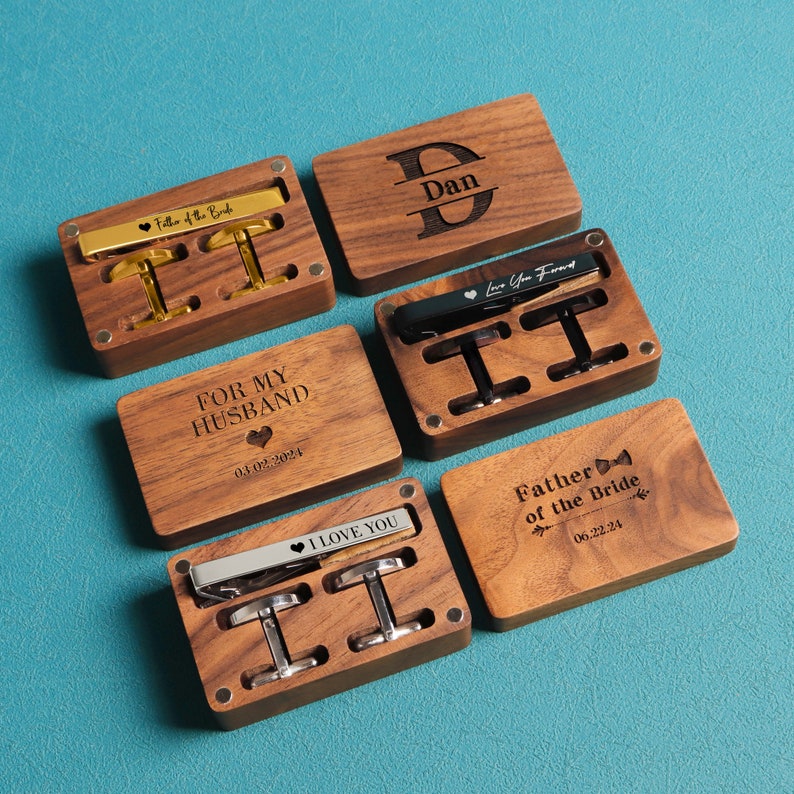 May include: Five wooden boxes with engraved messages and dates. Each box contains a tie clip and cufflinks. The messages include "For My Husband", "Father of the Bride", "Dan", "Love You Forever", and "Best Man".