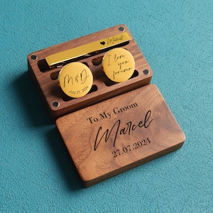 May include: A wooden box with a gold tie bar and two gold cufflinks. The cufflinks have the text "M&D July 27, 2024" and "I love you forever". The box has the text "To My Groom Marcel 27.07.2024".