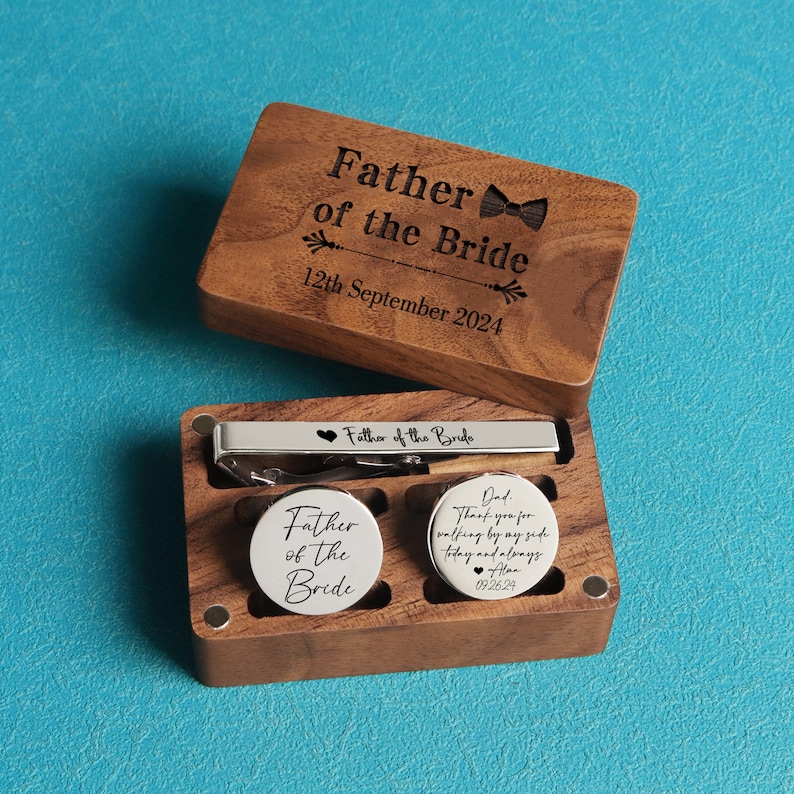 May include: A wooden box with a hinged lid containing a tie bar and two cufflinks. The box is engraved with the text "Father of the Bride" and the date "12th September 2024". The tie bar and cufflinks are also engraved with the text "Father of the Bride".