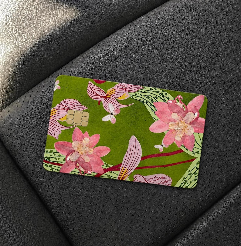 Puede incluir: Una tarjeta de cr&eacute;dito rectangular con un fondo verde oliva vibrante decorado con un patr&oacute;n repetitivo de grandes flores rosas estilo loto, follaje verde claro y peque&ntilde;as mariposas blancas, incluyendo un chip EMV dorado.