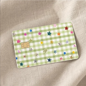 Puede incluir: Una tarjeta de cr&eacute;dito rectangular con un patr&oacute;n de cuadros vichy en verde claro y blanco. La superficie est&aacute; decorada con numerosas estrellas peque&ntilde;as y multicolores en tonos rosa, azul, amarillo y plateado. Se ve un chip EMV dorado.