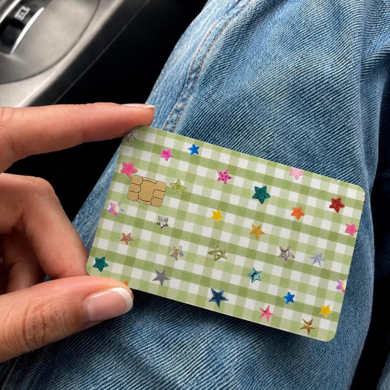 Puede incluir: Una tarjeta de pago rectangular que presenta un patr&oacute;n de cuadros vichy en color verde claro y blanco en toda la superficie. La tarjeta est&aacute; decorada con numerosas estrellas hologr&aacute;ficas peque&ntilde;as y multicolores y un chip EMV dorado.