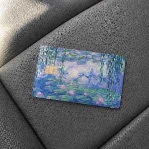May include: A rectangular credit card featuring a printed reproduction of an impressionist water lily painting. The design displays shades of blue, green, and purple with pink floral accents and hanging willow branches, including a gold EMV chip.