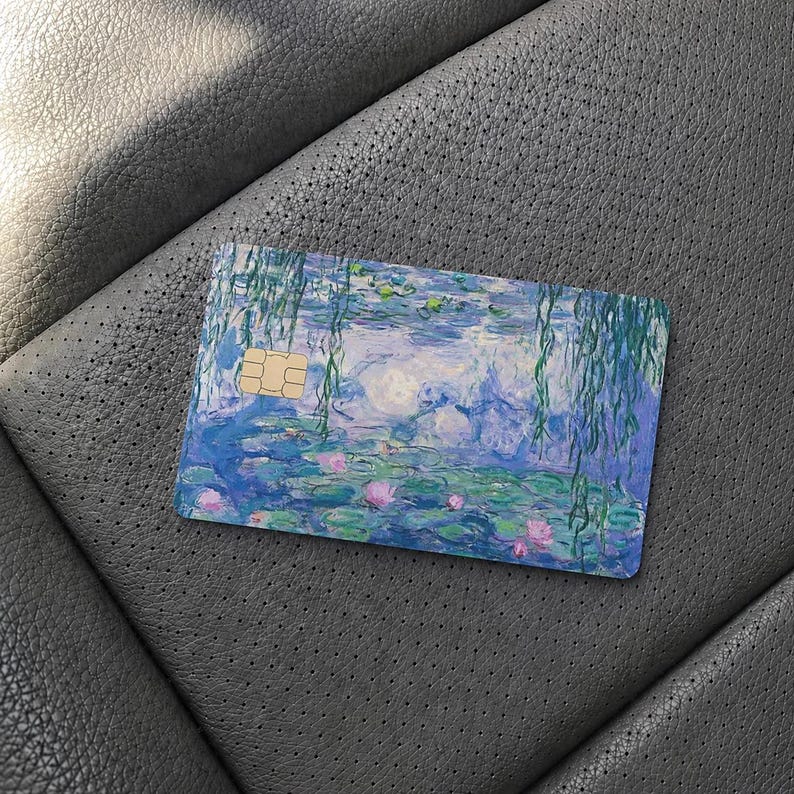May include: A rectangular credit card featuring a printed reproduction of an impressionist water lily painting. The design displays shades of blue, green, and purple with pink floral accents and hanging willow branches, including a gold EMV chip.