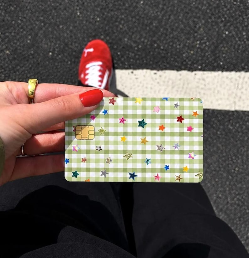 Puede incluir: Una tarjeta de cr&eacute;dito rectangular con un patr&oacute;n de cuadros vichy en verde claro y blanco, decorada con numerosas estrellas peque&ntilde;as, multicolores y hologr&aacute;ficas dispersas por la superficie, incluyendo un chip EMV dorado a la izquierda.