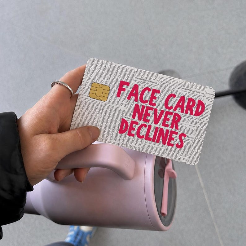 May include: A rectangular credit card skin featuring a newspaper print background with the bold, hot pink text "FACE CARD NEVER DECLINES" printed across the center. The skin includes a cutout for the gold EMV chip on the top left corner.
