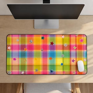 Puede incluir: Alfombrilla de ratón colorida con un patrón de cuadros en tonos rosa, amarillo, verde y morado. La alfombrilla está decorada con varias formas de estrellas brillantes. Un ratón de ordenador blanco está en el lado derecho.