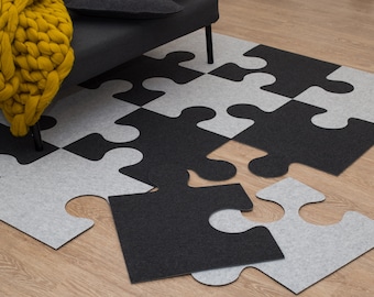 May include: A black and white puzzle rug made of felt. The rug is made up of individual puzzle pieces that fit together. The rug is laid out on a wooden floor.