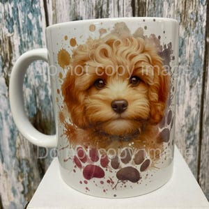 May include: White ceramic coffee mug featuring a watercolour design of a brown and white puppy with brown paw prints. The puppy is looking directly at the viewer.