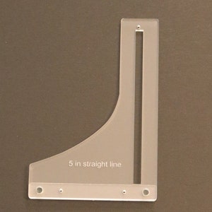 May include: A clear plastic ruler with a 5-inch straight line marking and a slot for a pencil. The ruler has four holes along the bottom edge.