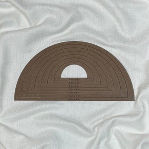 May include: A set of seven brown wooden half-circle stencils for crafting. The stencils are in graduated sizes, ranging from 4 inches by 2 inches to 16 inches by 8 inches. The sizes are printed on the stencils.