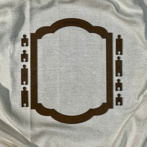 May include: A brown wooden frame with a scalloped top and sides. The frame is 11 inches by 8.5 inches and has a series of puzzle pieces on each side.