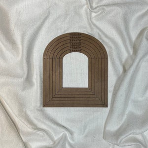 May include: A set of seven wooden arch-shaped stencils with measurements in inches. The stencils are arranged in a rainbow pattern, with the largest stencil at the top and the smallest stencil at the bottom. The stencils are made of brown wood and have a smooth finish.