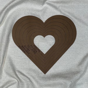 May include: A brown heart-shaped stencil with multiple concentric circles, each labeled with a different size in inches. The sizes are 4.5 in x 4 in, 6 in x 5.5 in, 7.5 in x 6.75 in, 9 in x 8 in, 10.5 in x 9.5 in, and 12 in x 11 in.