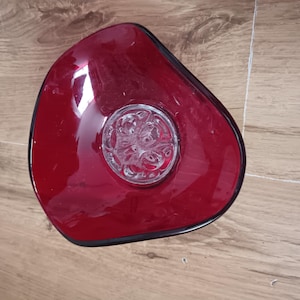 May include: A red glass bowl with a black rim and a clear, decorative centre. The bowl has an organic shape and sits on a wooden surface. The bowl is likely used for decorative purposes or serving.