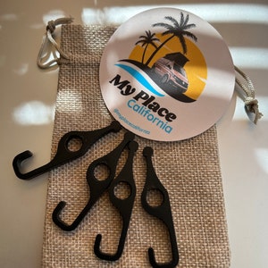 以下が含まれることがあります： 4つの黒い金属製のフックのセットで、各フックに小さな穴があります。フックは、小さな麻袋に入っています。麻袋には、ヤシの木とキャンピングカーのグラフィックが描かれた「My Place California」と書かれた丸いステッカーが付いています。ステッカーには「@myplacecalifornia」というテキストも含まれています。