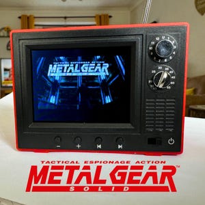 May include: A red and black retro-style television with a screen displaying the video game "Metal Gear Solid". The television has a knob for volume and a knob for tuning channels. The television also has buttons for power, play, pause, and rewind.