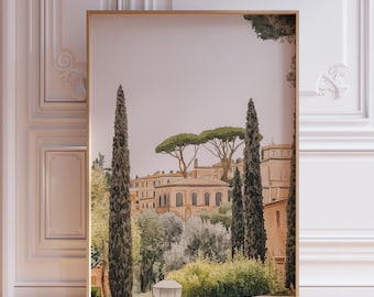 May include: A framed print of a watercolor painting depicting a cityscape with buildings and trees. The buildings are a pale peach color and the trees are a deep green. The sky is a soft pink.