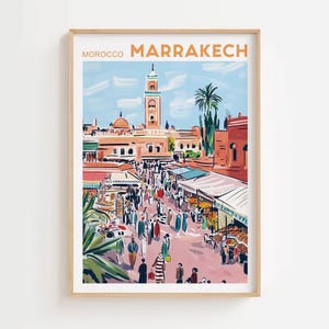 May include: A framed art print of Marrakech, Morocco, featuring a bustling marketplace scene. The artwork showcases a tall minaret, palm trees, and numerous figures in traditional attire. The color palette includes shades of orange, red, blue, and green.