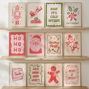 May include: A collection of framed Christmas-themed art prints displayed on wooden shelves. The prints feature festive illustrations and text, including a nutcracker, Santa Claus, and the phrase "Baby It's Cold Outside."