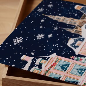 May include: A blue and white Christmas-themed gift box with a snowy village scene and a pink building with a red bow. The box is open and the lid is propped up.