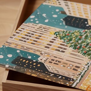 May include: A painting of a snowy city scene with tall buildings, a large Christmas tree, and falling snow. The buildings are lit up with warm yellow lights, and the snow is falling softly on the ground.
