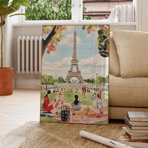 May include: A framed illustration of the Eiffel Tower in Paris, France. The illustration features a picnic scene with people sitting on a red and white checkered blanket in front of the tower. The illustration is in a vintage style with a watercolor effect.