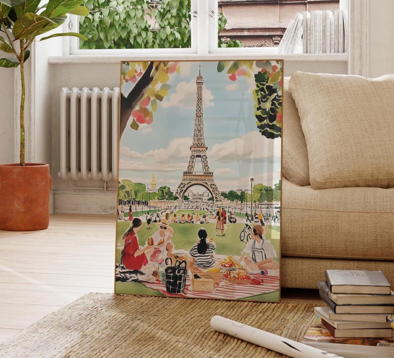 May include: A framed illustration of the Eiffel Tower in Paris, France. The illustration features a picnic scene with people sitting on a red and white checkered blanket in front of the tower. The illustration is in a vintage style with a watercolor effect.