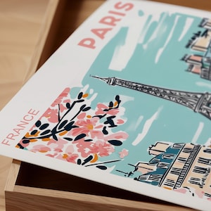 May include: A white and blue illustration of the Eiffel Tower in Paris, France. The illustration includes pink cherry blossoms and the text "PARIS" and "FRANCE".