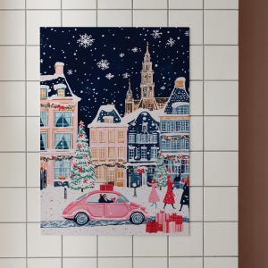 May include: A pink vintage car drives through a snowy European town at night. The car is decorated with a red bow and a Christmas tree is visible in the background. The town is decorated with Christmas lights and snow is falling.