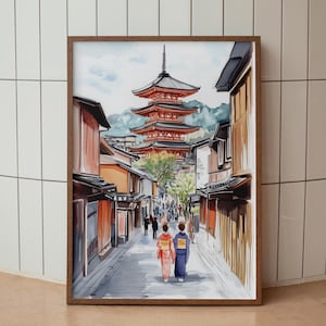 May include: Watercolor print of a Japanese street scene with a red pagoda in the background. Two figures in traditional clothing walk down a cobblestone street lined with buildings. The artwork is framed in a brown wooden frame.