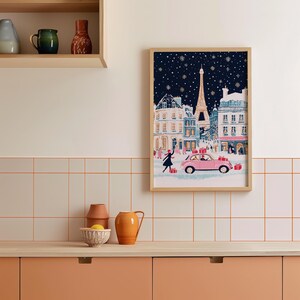 K&ouml;nnte beinhalten: Eine gerahmte Illustration einer verschneiten Pariser Stra&szlig;enszene mit dem Eiffelturm im Hintergrund. Die Illustration zeigt ein rosa Auto mit Menschen, die Geschenke tragen, und eine Frau in einem blauen Kleid, die auf dem Schnee Schlittschuh l&auml;uft.