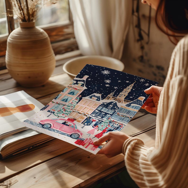 May include: A colorful illustration of a snowy European city scene with a pink car driving down a street lined with buildings. The illustration is printed on a white card.