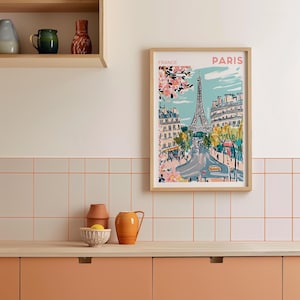May include: A framed illustration of the Eiffel Tower in Paris, France. The illustration is in a colorful, cartoon style and features a blue sky, green trees, and pink flowers. The text "FRANCE" and "PARIS" is printed at the top of the illustration.