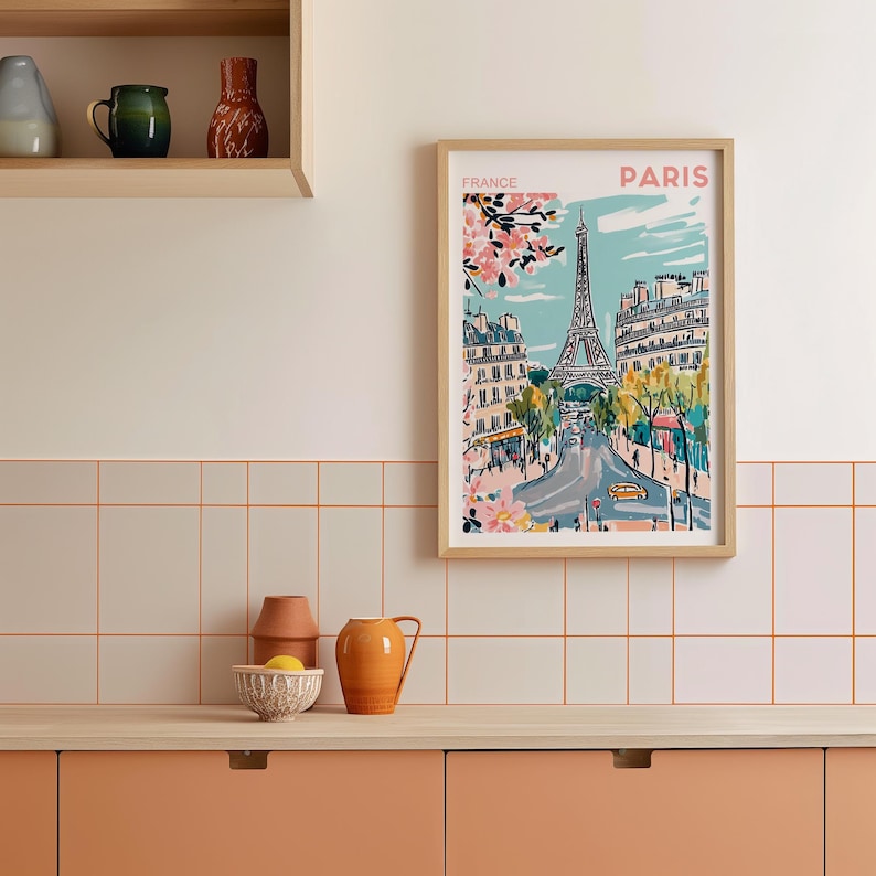 May include: A framed illustration of the Eiffel Tower in Paris, France. The illustration is in a colorful, cartoon style and features a blue sky, green trees, and pink flowers. The text "FRANCE" and "PARIS" is printed at the top of the illustration.
