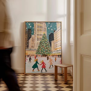 May include: A framed painting of a snowy city scene with a large Christmas tree in the center. People are ice skating on a rink in front of the tree. The buildings are tall and decorated with lights. The painting is in a modern style with bright colors and bold lines.