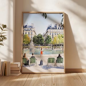 May include: A watercolor painting of a Parisian park scene with a fountain, trees, and people sitting on benches. The painting is framed in a light wood frame.