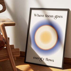 May include: A framed print with a white background and a blue and orange circle in the center. The text "Where focus goes energy flows" is printed below the circle.