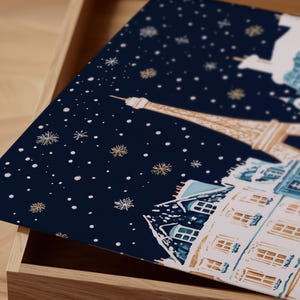 K&ouml;nnte beinhalten: Eine marineblaue Box mit einem Design einer verschneiten Pariser Stadtlandschaft. Der Eiffelturm ist im Hintergrund zu sehen, mit Geb&auml;uden und Schneeflocken im Vordergrund.