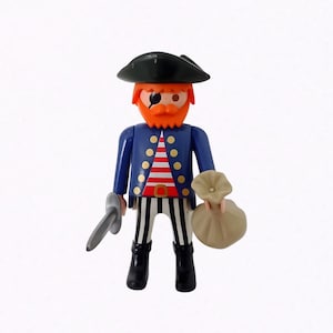 Op de afbeelding: Een speelgoed piratenfiguur met een zwarte hoed, blauwe jas en gestreepte broek. De piraat heeft een oranje baard, een ooglapje en houdt een zwaard en een beige zak vast. Klassiek speelgoed.