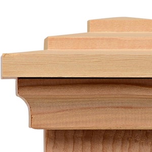 May include: A natural wood post cap with a layered, tiered design. The cap has a square base and a flat top.