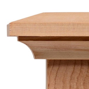 May include: A wooden post cap with a square top and a decorative molding around the edge. The cap is made of unfinished wood and has a natural wood grain.