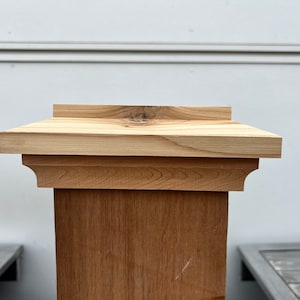 May include: A wooden post with a decorative top. The post is made of light brown wood and the top is made of a lighter wood with a slightly different grain.