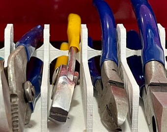 Puede incluir: Un organizador de herramientas blanco impreso en 3D que contiene varias herramientas manuales, incluyendo alicates y destornilladores. Las herramientas tienen mangos azules, amarillos y negros. El organizador está dentro de un cajón rojo de caja de herramientas.