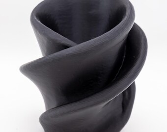 Puede incluir: Un jarrón de cerámica negro con un diseño único y arremolinado. El jarrón tiene una superficie texturizada y una parte superior curva y abierta. El color oscuro y la forma orgánica le dan un toque moderno y artístico.
