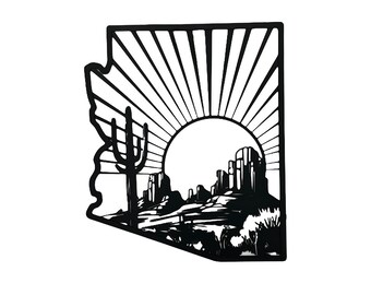 Puede incluir: Pieza de arte en metal blanco y negro con la forma de Arizona, que presenta un paisaje desértico con un sol naciente y un cactus saguaro. El diseño es una silueta, con los rayos del sol que emanan de detrás de las montañas.