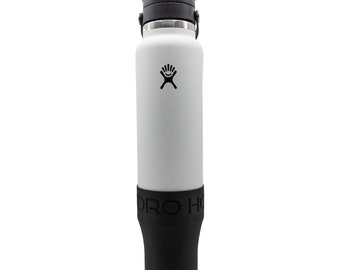 Puede incluir: Una botella de agua aislada blanca con tapa y base negras. La botella tiene un logotipo negro y una funda de silicona negra en la parte inferior. La botella está diseñada para mantener las bebidas frías o calientes. La botella mide aproximadamente 23 cm de alto.
