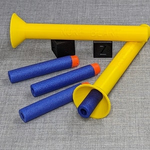 Könnte beinhalten: Vier blaue und orangefarbene dartartige Objekte und zwei gelbe Plastikspielzeugpistolen. Eine Pistole hat den Schriftzug "NUKLEAR BLAST" aufgedruckt.